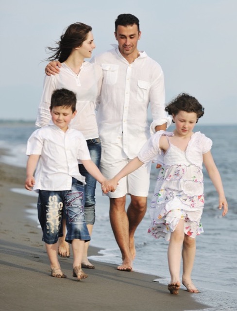 Picture of a family walking on a beach, with a mother & father and their young son & daughter